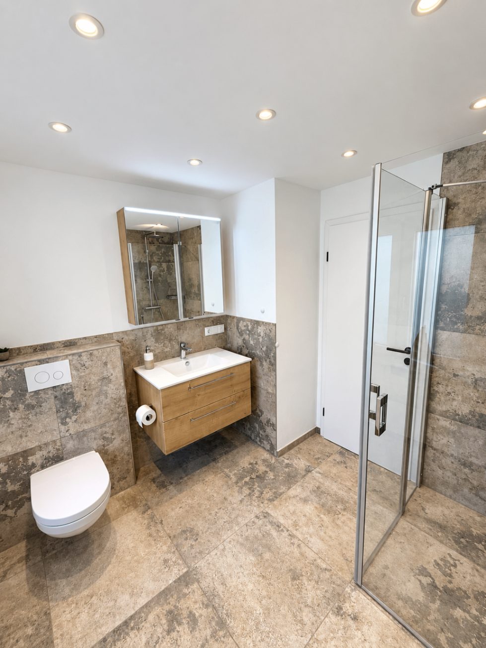 Badezimmer der Ferienwohnung Liserl mit bodengleicher Glasdusche und Steinfliesen