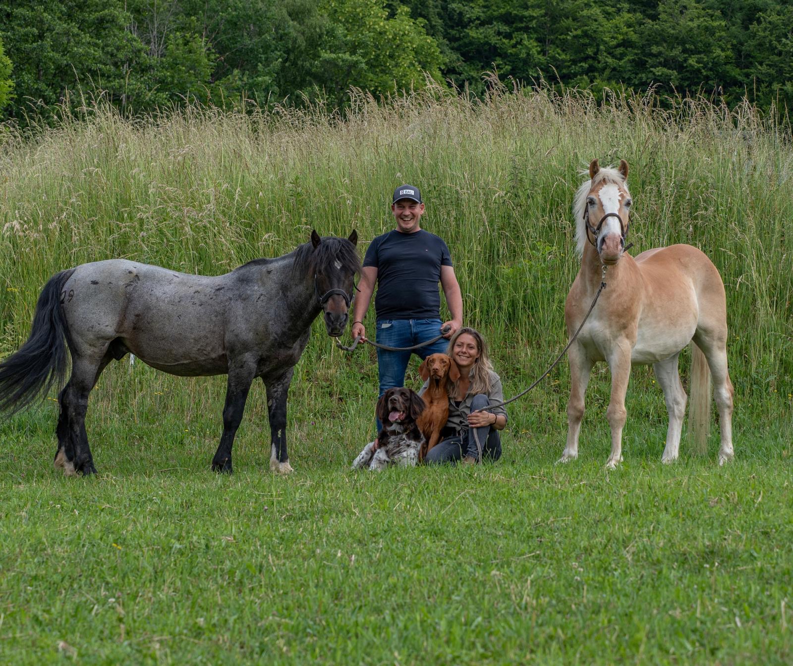 Gastgeber Sebastian Lemberger mit seiner Partnerin, zwei Pferden und zwei Hunden auf der Wiese am Hof in Lalling